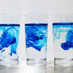 Three glasses each with a blue food dye swirling around