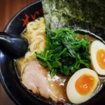 A perfect bowl of japanese ramen with a full boiled egg, pork, and a oily broth in a black bowl