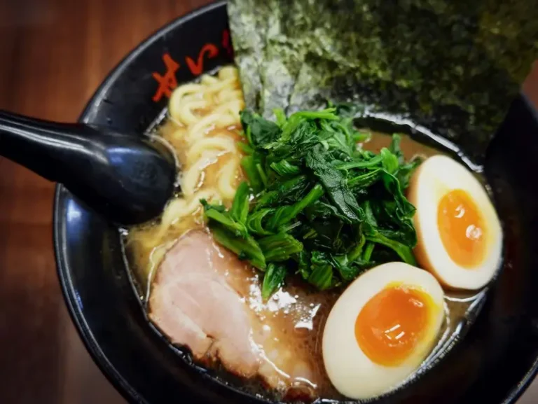 A perfect bowl of japanese ramen with a full boiled egg, pork, and a oily broth in a black bowl