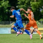Two football players. One wearing a blue kit and one wearing an orange kit