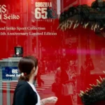 A woman wlaking past a window advertisment for godzilla