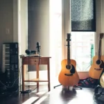 An apartment with sunlight shining through the window onto two acoustic guitars