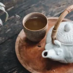 A cup of black tea next to a white ceramic kettle