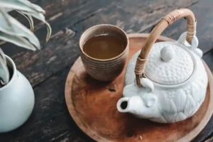 A cup of black tea next to a white ceramic kettle