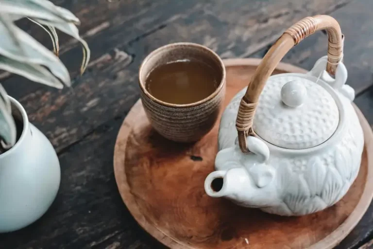 A cup of black tea next to a white ceramic kettle