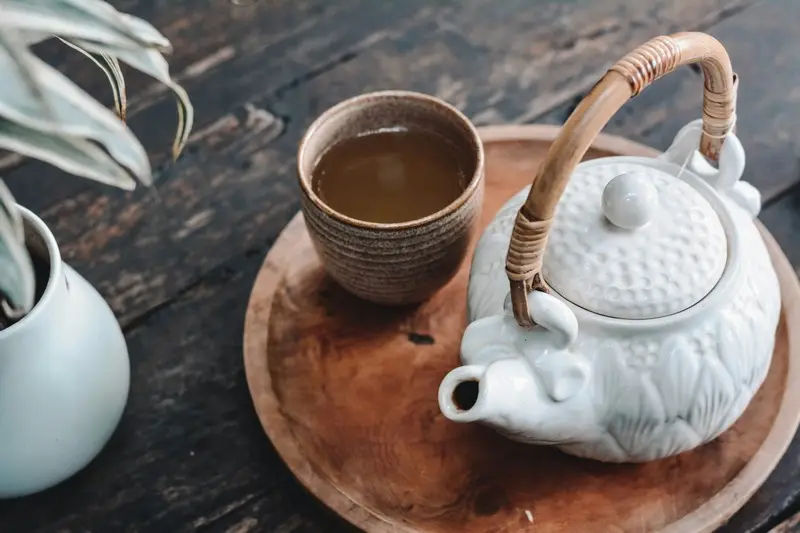 A cup of black tea next to a white ceramic kettle