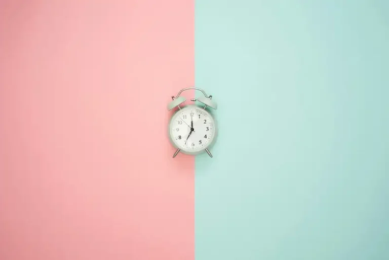 An alarm clock against a background of pastel pink and blue