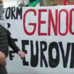A protestor at the eurovision song contest in front of a banner saying 'genocide eurovision'.