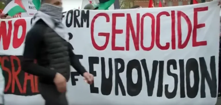 A protestor at the eurovision song contest in front of a banner saying 'genocide eurovision'.