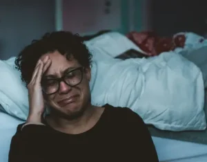 A woman crying next to a bed
