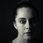 A woman in tears against a black background.