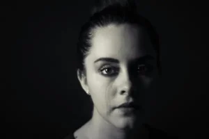 A woman in tears against a black background.