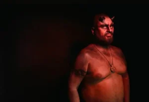 A man in the dark draped in a red hue with horns. Looks like the devil.