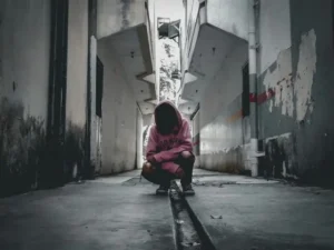 A person kneeling down against a grey urban backdrop.