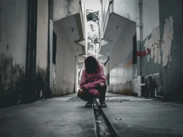A person kneeling down against a grey urban backdrop.