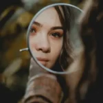 A woman looking into a round mirror.