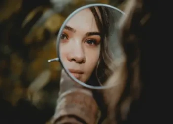 A woman looking into a round mirror.