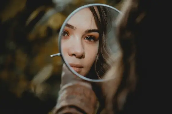 A woman looking into a round mirror.