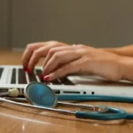 A clinical social worker typing on a laptop with a stethoscope next to it