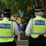 Two british police viewed from behind wearing yellow vests