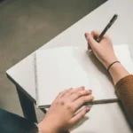 Somebody writing an essay by hand on a notepad
