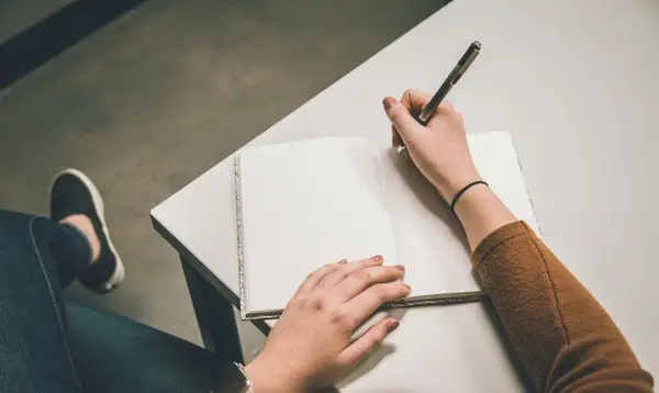 Somebody writing an essay by hand on a notepad