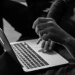 Somebody typing an essay on a laptop in black and white