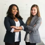 Two professional women with their arms crossed smiling.