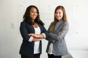Two professional women with their arms crossed smiling.