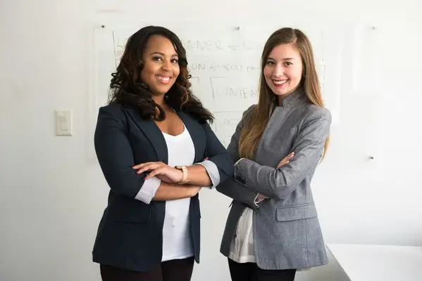 Two professional women with their arms crossed smiling.