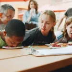 Kids having a school dinner with one kid putting their head in their food