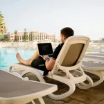 A man on his laptop on a sunlounger by the pool