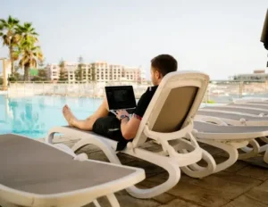 A man on his laptop on a sunlounger by the pool