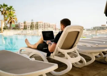 A man on his laptop on a sunlounger by the pool