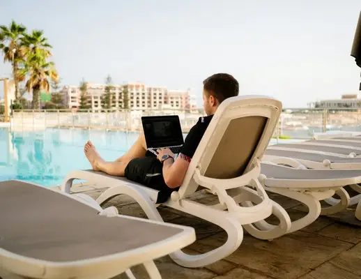 A man on his laptop on a sunlounger by the pool