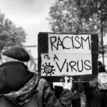 Black and white shot of a protest placard which reads "racism is a virus".