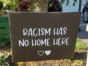 A black placard with 'racism has no home here' written in white