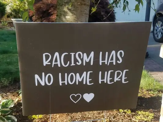 A black placard with 'racism has no home here' written in white