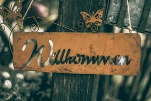A brown sign hung on a tree saying 'wilkommen'.