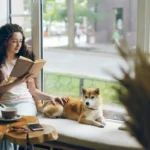 A woman reading a book in the window recess with her dog.
