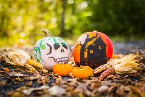 Two expertly decorated pumpkins. one is white with a scary face and the other is orange with a haunted house.