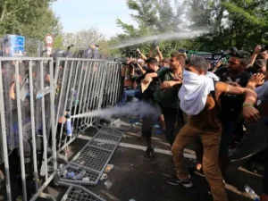 A large group of migrants at a security checkpoint being sprayed with gas