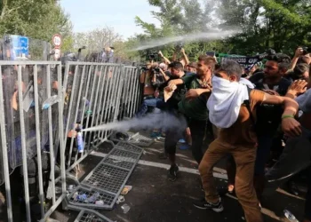 A large group of migrants at a security checkpoint being sprayed with gas