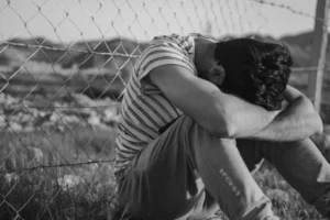 Black and white shot of a person sitting on the floor with their head in their arms.