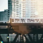 An urban vista with a train crossing a bridge in front of high rise buildings