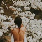a woman with her back naked against tree blossoms