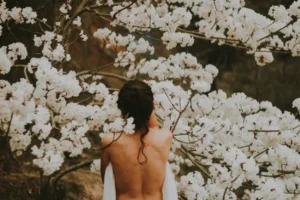 a woman with her back naked against tree blossoms