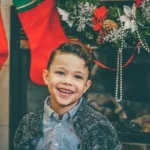A smiling child at christmas in front of the fireplace with stockings hung up.