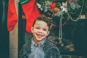A smiling child at christmas in front of the fireplace with stockings hung up.