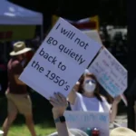 A feminist holding a placard saying 'i will not go back to the 1950's'.